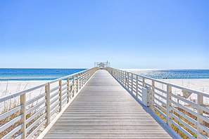 Eine hölzerne Steg, der zu einem Strand mit blauem Himmel führt.
