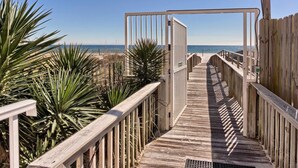 A wooden boardwalk leading to a beach with palm trees and a clear sky. - Gulf-front condo w/ beach access, indoor/outdoor pool, & tennis courts (Orange Beach)