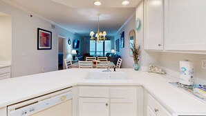 A modern kitchen with a central island, recessed ceiling lights, and a dining area in the background. - Gulf-front condo w/ beach access, indoor/outdoor pool, & tennis courts (Orange Beach)
