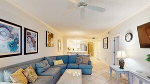 A living room with a sectional sofa, a coffee table, a ceiling fan, and artwork on the walls. - Gulf-front condo w/ beach access, indoor/outdoor pool, & tennis courts (Orange Beach)