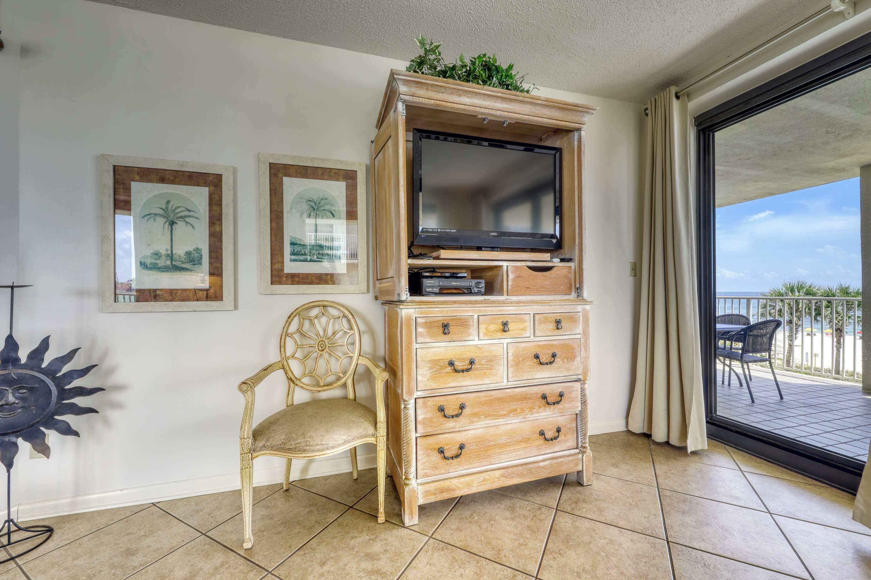 A room with a wooden cabinet, a television, a chair, and framed pictures on the wall.