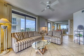 A spacious living room with striped sofas, a glass coffee table, and a ceiling fan. - Gulf Front Condo with Shared Pools, Hot Tub, Tennis, & Fitness Room (Orange Beach)