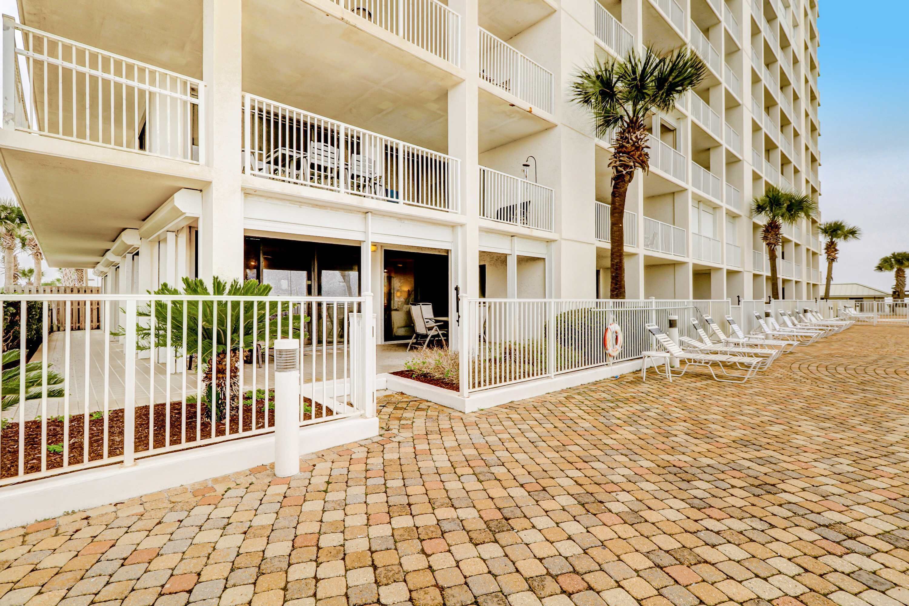 A multi-story hotel with balconies, a paved walkway, and outdoor seating.
