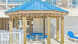 A wooden deck with a gazebo, a lounge chair, and a sign. - Gulf front condo with onsite snack bar, three shared pools, and internet (Orange Beach)