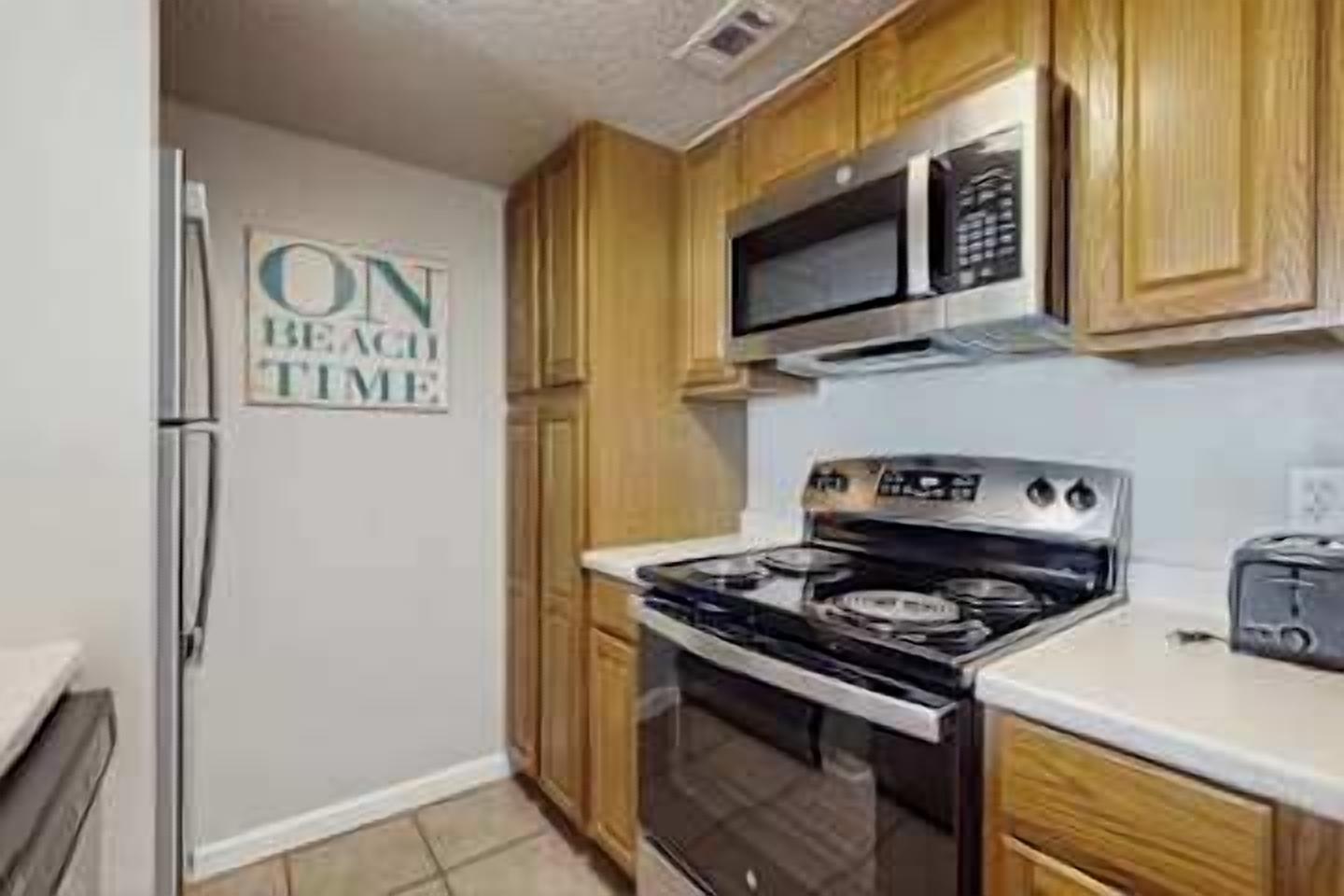 A kitchen with wooden cabinets, a stainless steel refrigerator, a microwave, an oven, and a toaster.