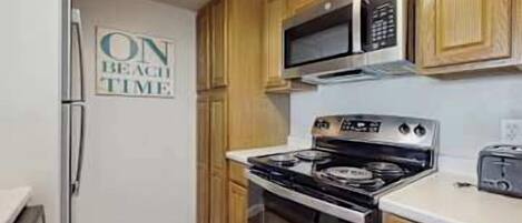 Eine Küche mit Holzausstattung, einem Edelstahlkühlschrank, einer Mikrowelle, einem Backofen und einem Toaster.