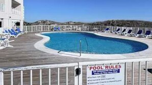 A pool with a sign indicating rules, surrounded by lounge chairs and a wooden deck. - Gulf front condo with onsite snack bar, three shared pools, and internet (Orange Beach)