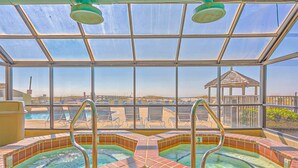 Een hottub in een glazen omkasting met vrij uitzicht op het zwembad en een gazebo op de achtergrond.