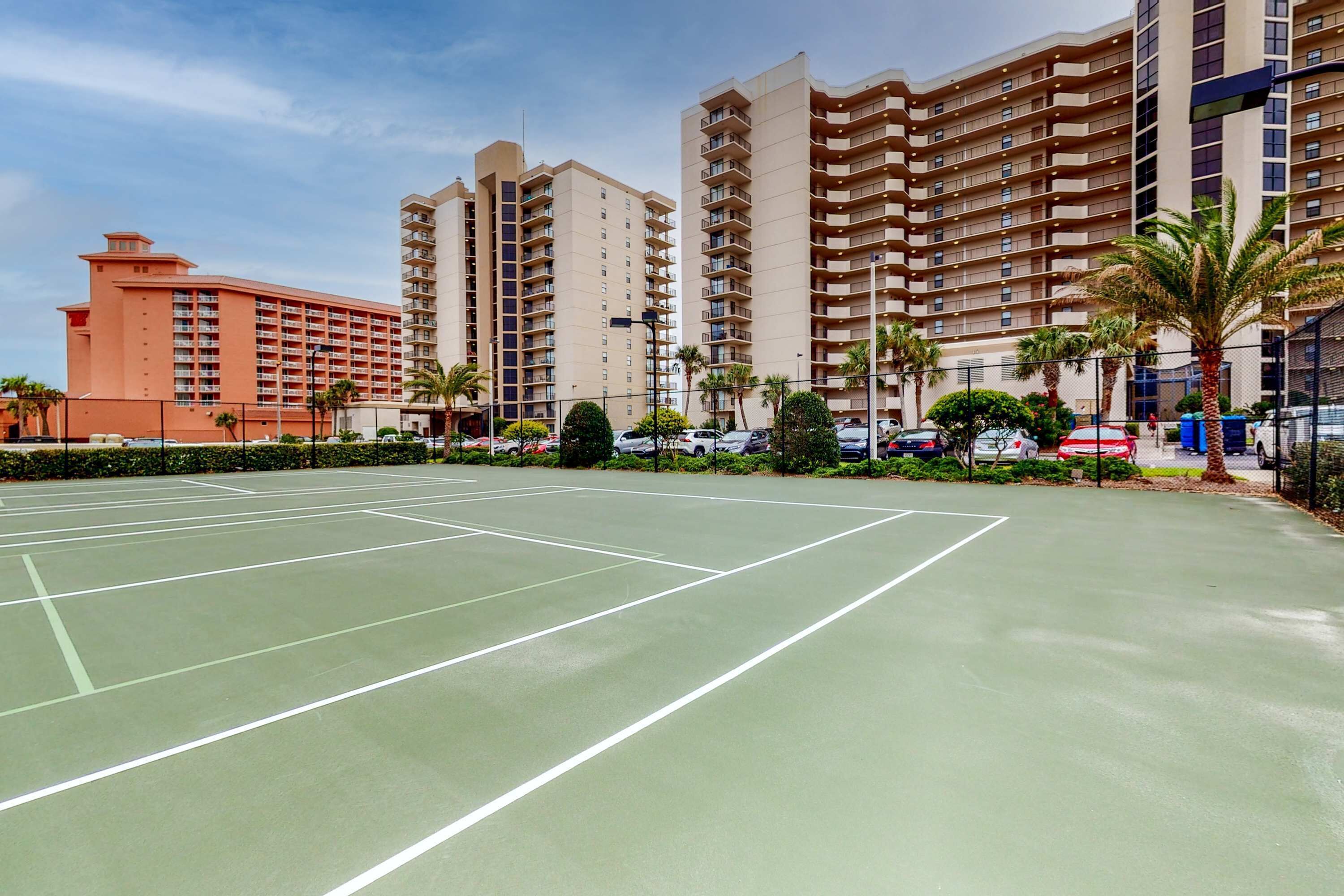 A tennis court with surrounding buildings, including a hotel and residential apartments.