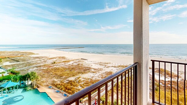 Een balkon met uitzicht op een strand, een zwembad en een steiger.