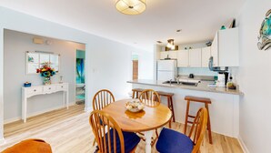 Een moderne keuken met witte kasten, een centraal eiland en een eethoek met een houten tafel en stoelen.