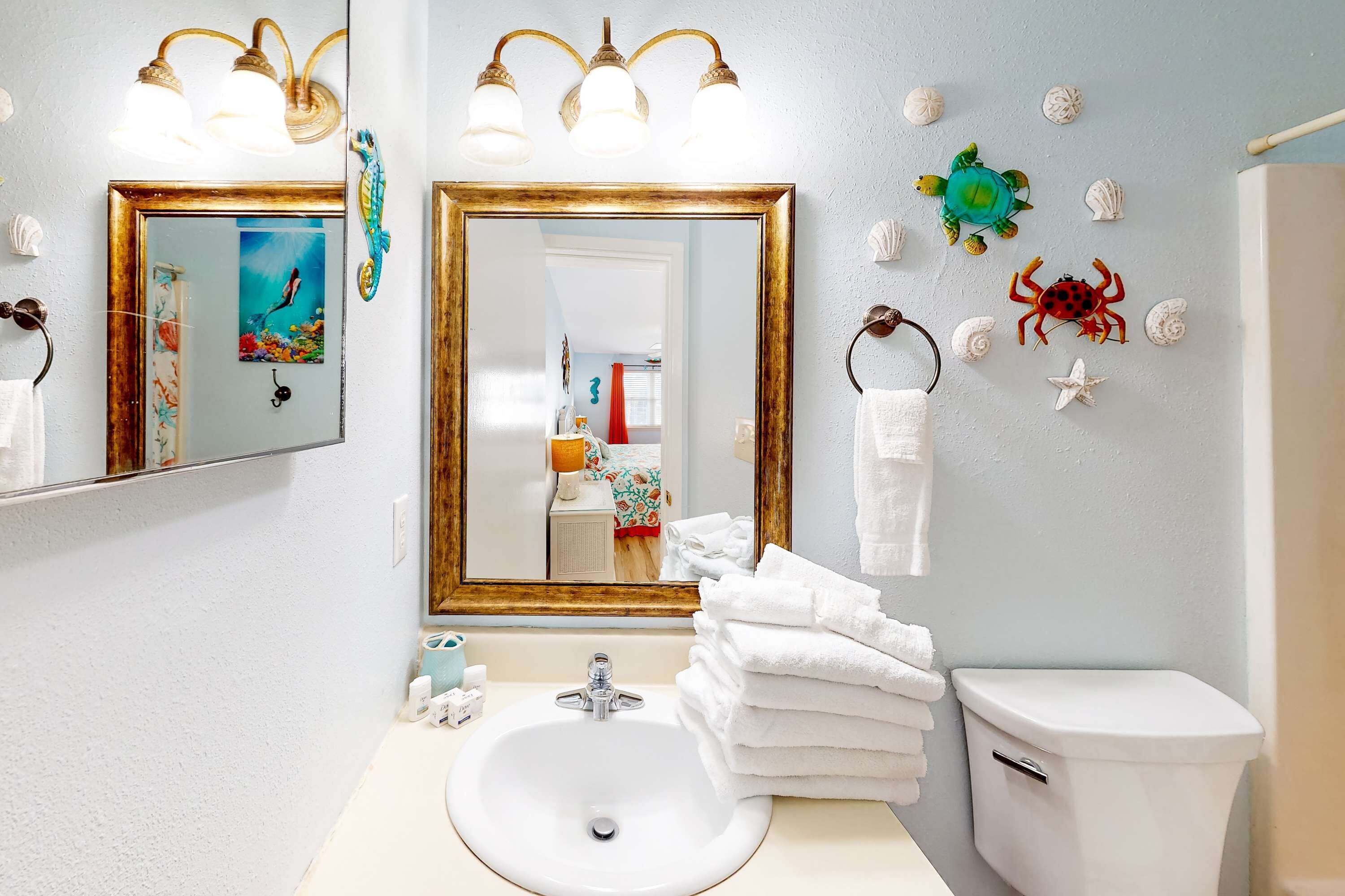 A bathroom with a sink, toilet, and two mirrors with light fixtures.