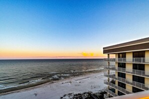 Ein Strandhotel mit Balkon und Blick auf den Ozean, einem Sandstrand und einem wolkenlosen Himmel.