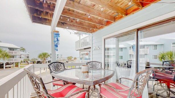An outdoor patio with a glass table and chairs, a wooden ceiling, and a view of other buildings. - Calming water view condo with full kitchen, balcony, pool, & TV - close to park (Orange Beach)