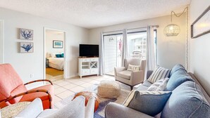A living room with a sofa, armchair, ottoman, television, and artwork on the walls. - Calming water view condo with full kitchen, balcony, pool, & TV - close to park (Orange Beach)