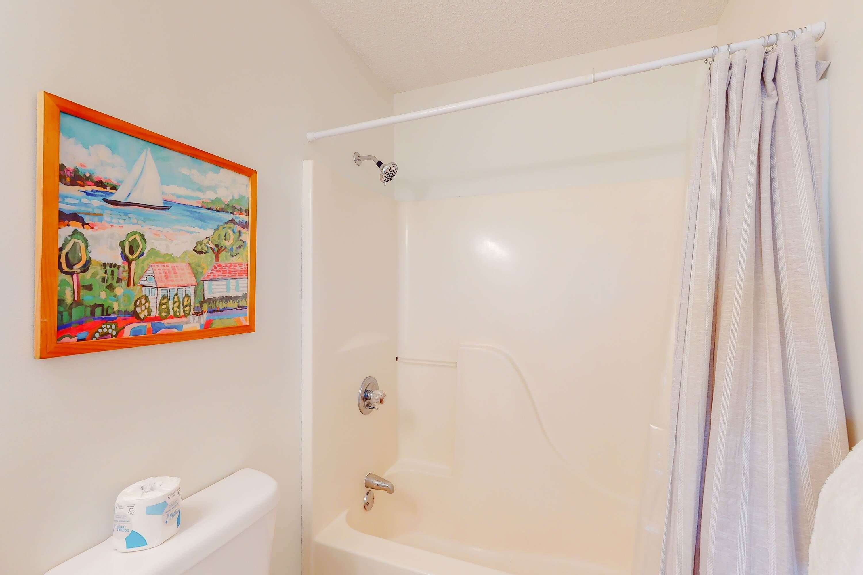 A bathroom with a bathtub, a showerhead, a toilet, and a painting on the wall.