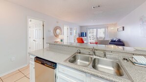 A kitchen with a dishwasher, double sink, and a countertop. - Calming water view condo with full kitchen, balcony, pool, & TV - close to park (Orange Beach)