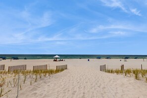 Une plage de sable avec une clôture en bois, un parasol blanc et un ciel bleu dégagé.