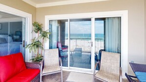 Ein Balkon mit Blick auf den Strand, eine rote Couch, Korbstühle und ein Topf mit Pflanze.
