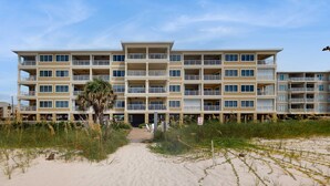 Ein mehrstöckiges Hotel mit Balkonen, ein Sandstrand davor und eine Palme.