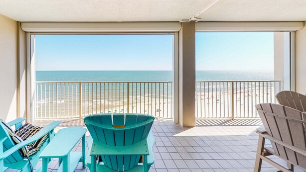 Ein Balkon mit Blick auf den Strand, zwei Stühle und ein Tisch.