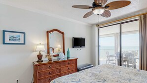 Ein Schlafzimmer mit Bett, Kommode, Spiegel, Fernseher und einem Balkon mit Stühlen.