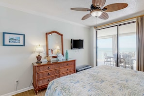 A bedroom with a bed, dresser, mirror, TV, and a balcony with chairs. - White Caps | Beachfront | Pools, Hot Tub & Tennis | Gulf-View Balcony (Orange Beach)