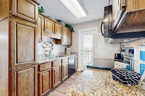 A kitchen with wooden cabinets, granite countertops, a stainless steel range hood, and a dishwasher. - First floor condo with shared pool, close to the beach, and washer & dryer (Gulf Shores)