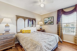 A bedroom with a bed, two bedside tables, a nightstand, a ceiling fan, a window with curtains, and a painting on the wall. - First floor condo with shared pool, close to the beach, and washer & dryer (Gulf Shores)