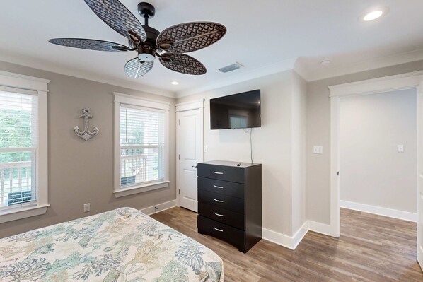 Une chambre à coucher avec un lit, une commode, un ventilateur de plafond, une télévision et une fenêtre.