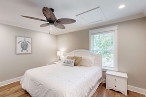 A bedroom with a bed, a nightstand, a ceiling fan, a window, and a framed picture on the wall.
