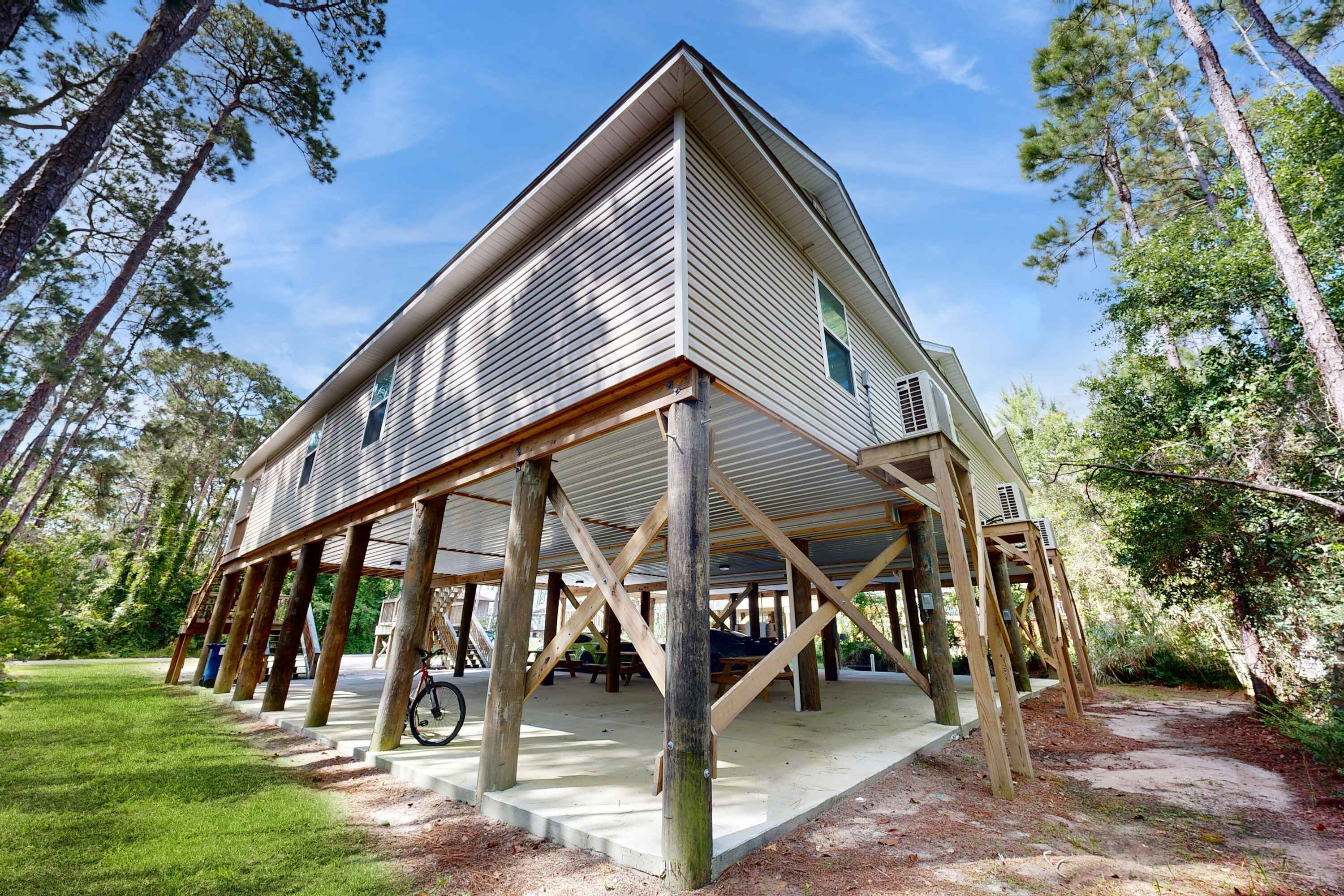A two-story wooden house with a porch supported by wooden beams, surrounded by trees.