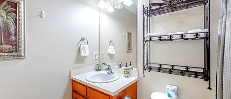 A bathroom with a sink, mirror, towel rack, toilet, and a framed picture on the wall.