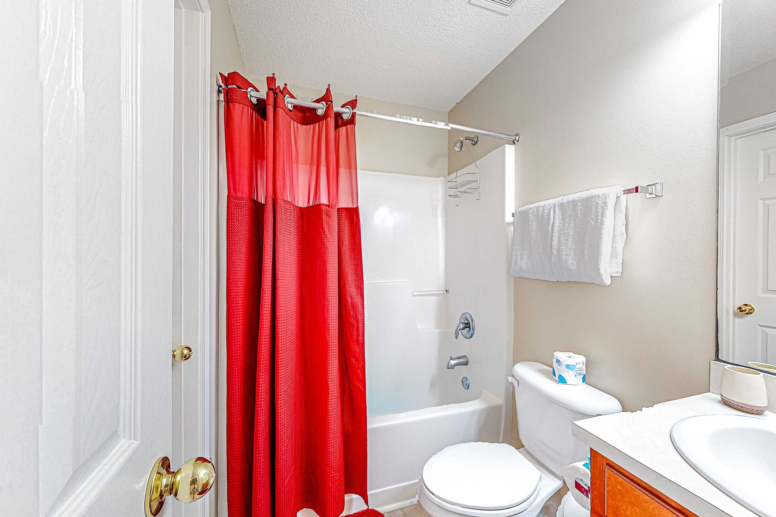 A bathroom with a white bathtub, a white toilet, a red shower curtain, and a white sink.