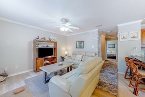 Una sala de estar con sofá, televisor, mueble de entretenimiento de madera y una zona de comedor con sillas.