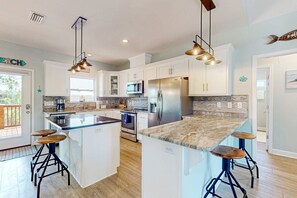 A modern kitchen with white cabinets, stainless steel appliances, and a central island with stools. - Dog friendly coastal home with beach access, pool, pickleball & golf nearby (Dauphin Island)