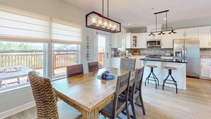 Une cuisine moderne avec des meubles blancs, un îlot central doté de tabourets et un coin repas avec une table et des chaises en bois.