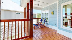 Une véranda couverte avec des balustrades en bois, une terrasse en bois et deux fauteuils de jardin bleus.