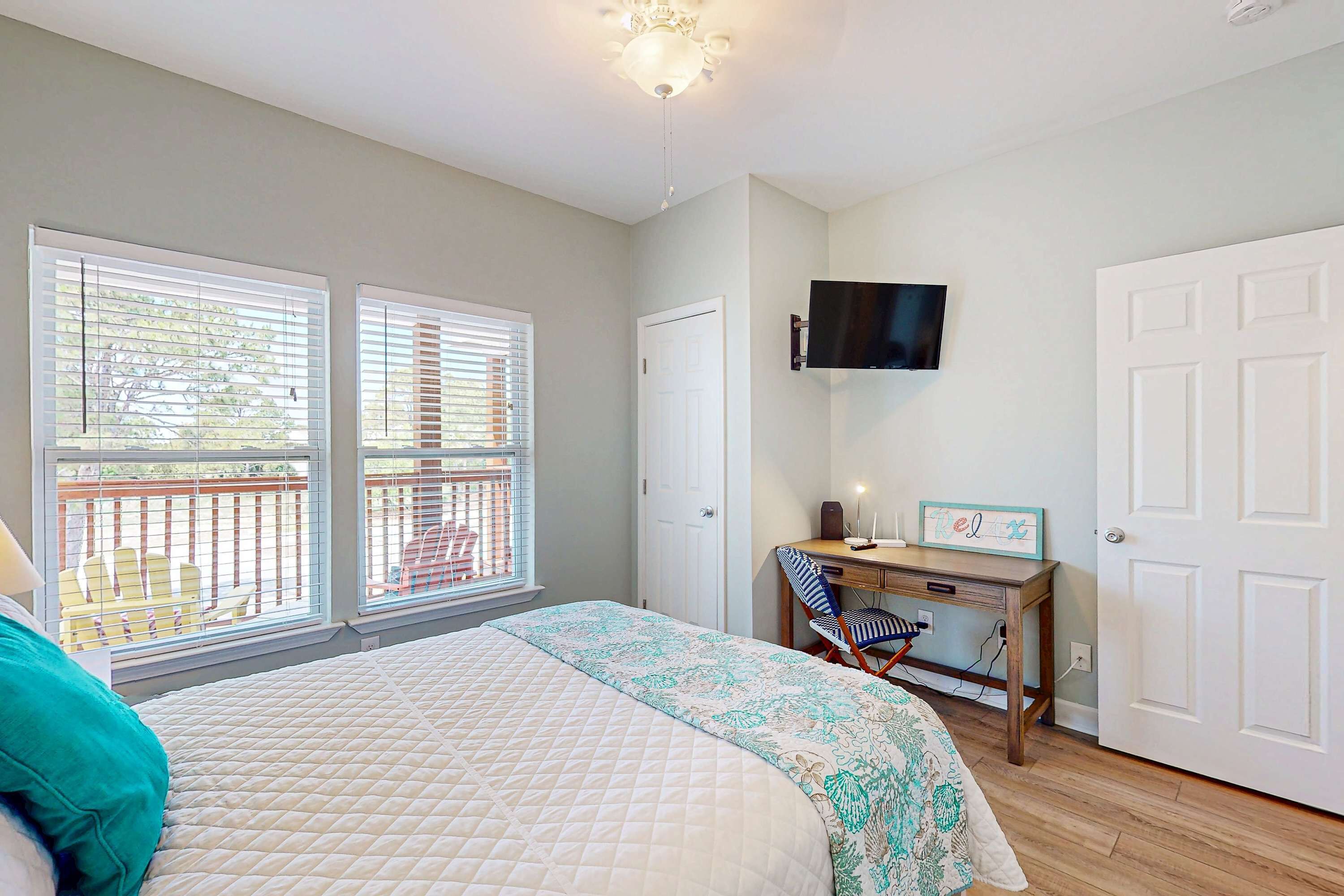 A bedroom with a bed, a desk, a chair, a TV, and a balcony.