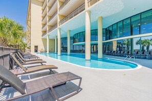 A pool area with lounge chairs and a large building with balconies. - Beachfront condo with indoor & outdoor pools, hot tub, fitness center, tennis (Dauphin Island)