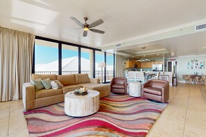 A spacious living area with a sofa, armchairs, a coffee table, and a large window with a view. - Beachfront condo with indoor & outdoor pools, hot tub, fitness center, tennis (Dauphin Island)
