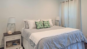 Un dormitorio con cama, mesitas de noche, lámpara, cortina y una pequeña estatua.