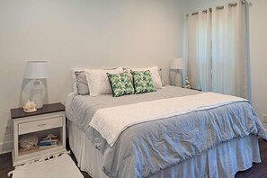 A bedroom with a bed, nightstands, a lamp, a curtain, and a small statue. - Cozy cottage located near the beach with gas grill, yard, & washer & dryer (Dauphin Island)