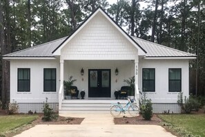 A white single-story house with a front porch, two windows on each side, and a bicycle parked in front. - Cozy cottage located near the beach with gas grill, yard, & washer & dryer (Dauphin Island)