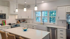 Una cocina moderna con armarios blancos, electrodomésticos de acero inoxidable, una isla central e iluminación colgante.
