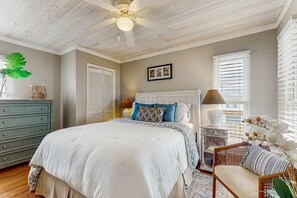 Une chambre à coucher comprenant un lit, une commode, une chaise, une lampe et une fenêtre avec des stores.