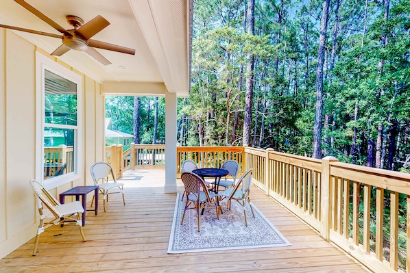 A wooden deck with a table and chairs, a ceiling fan, and a view of a forest.