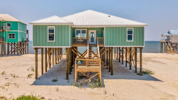 A beachfront wooden structure with a staircase, a door, and a sign indicating room number 106. - Exquisite oceanfront beach home with hot tub, central AC, balcony, & W&D (Dauphin Island)