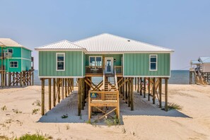 Een houten gebouw aan het strand met een trap, een deur en een bord met daarop kamer 106.