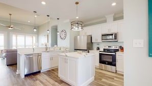 A spacious kitchen with white cabinetry, a central island, stainless steel appliances, and pendant lighting. - Exquisite oceanfront beach home with hot tub, central AC, balcony, & W&D (Dauphin Island)